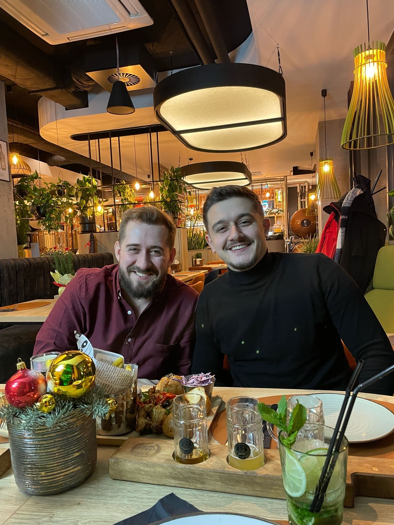 Dwóch uśmiechniętych mężczyzn w restauracji, przed nimi deska z piwami do degustacji