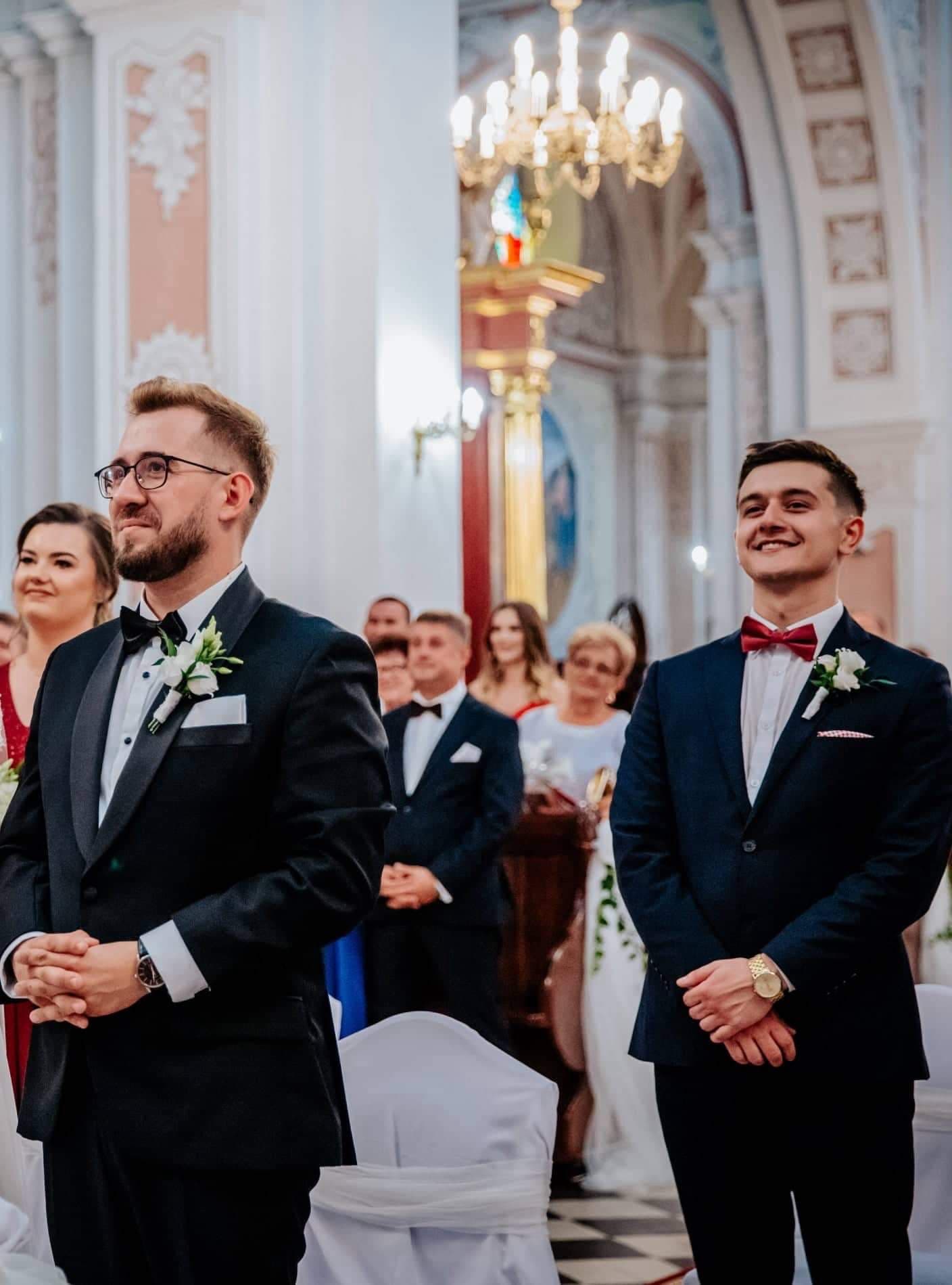 Ceremonia w kościele — wzruszony pan młody, obok uśmiechnięty świadek w czerwonej musze
